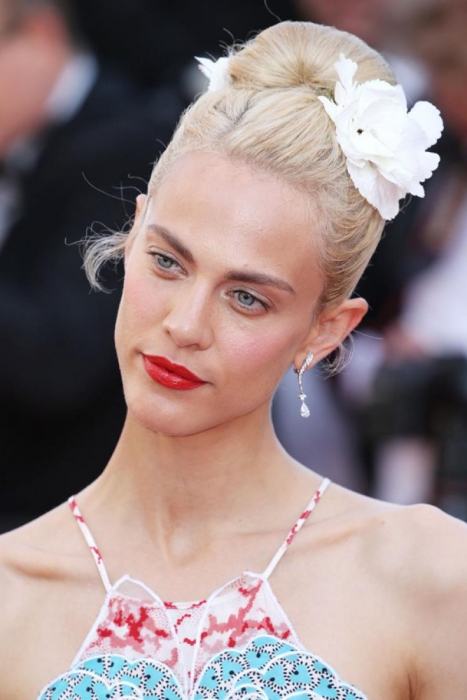 Довершали образ звезды фильма «Сен-Лоран. Стиль это я» Эймелин Валейде высокая прическа, обрамленная массивной заколкой в форме цветка, и ярко-алые