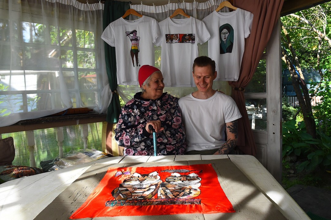 Юлия вместе с внуком Яном на фоне футболок со своими работами