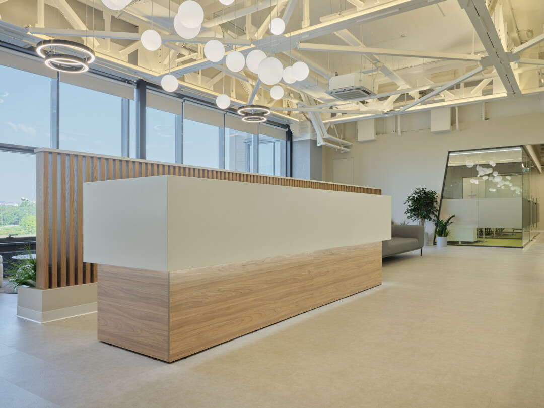 Стойка ресепшен в светлых тонах со столешницей из акрилового камня и подсветкой органично вписывается в концепцию эколофта. Диваны цвета «стоун» в