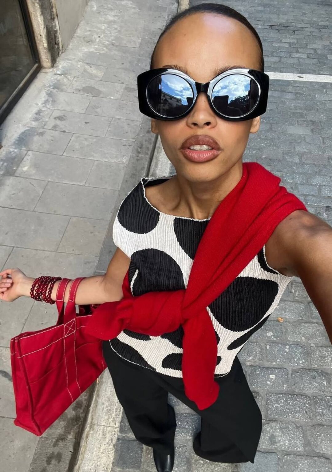 Инфлюенсер Кристина Чени голосует за гранд-горошины и разбавляет черно-белый образ ярко-красными деталями — джемпером, браслетом и сумкой